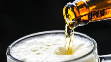 Dettaglio di una bottiglia di birra che verso schiuma densa in un boccale trasparente su sfondo scuro