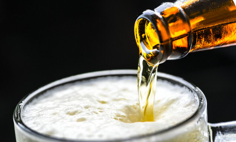 Dettaglio di una bottiglia di birra che verso schiuma densa in un boccale trasparente su sfondo scuro