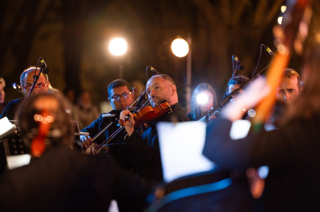 Primo piano di un violinista in abito scuro impegnato a suonare durante lo spettacolo allaperto di Opera Camion illuminato da luci calde sullo sfondo - attualita.it Primo piano di un violinista in abito scuro impegnato a suonare durante lo spettacolo allaperto di Opera Camion illuminato da luci calde sullo sfondo