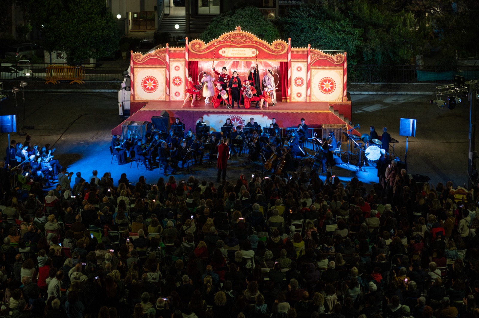 Veduta dallalto del camionteatro aperto che ospita Il barbiere di Siviglia con orchestra e cantanti e il pubblico seduto allaperto