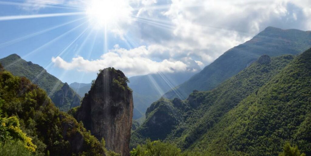 Veduta panoramica del Parco Nazionale del Pollino a Orsomarso, con imponente picco roccioso al centro e raggi di sole tra le montagne verdi della Calabria