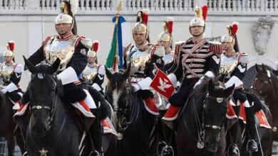 Ceremonial cavalry parade: armored riders on black horses, wearing ornate helmets and uniforms, carrying flags.